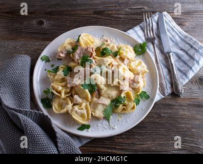 Tortellini alla panna.Plat traditionnel de pâtes italiennes fraîches et cuites.Servi sur une plaque blanche isolée sur fond de table en bois Banque D'Images