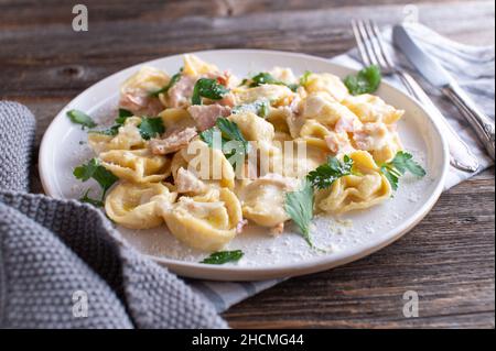 Tortellini alla panna.Plat traditionnel de pâtes italiennes fraîches et cuites.Servi sur une plaque blanche isolée sur fond de table en bois Banque D'Images