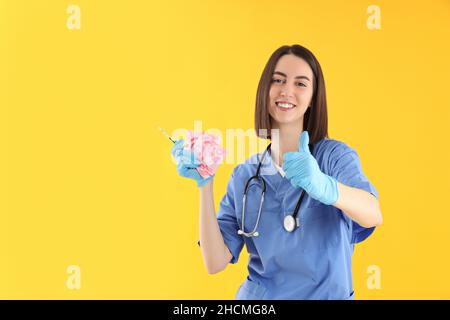 Infirmière féminine avec électrodes et test de grossesse sur fond jaune Banque D'Images