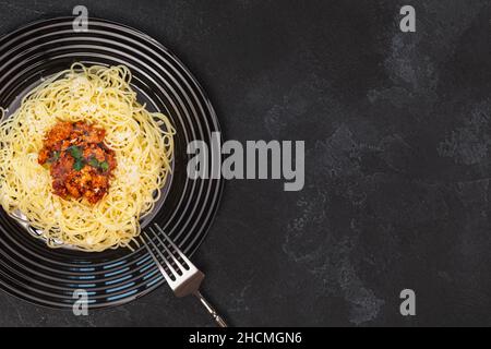 Bolognaise traditionnelle à spaghetti.Composition alimentaire avec pâtes chaudes dans une assiette noire avec fourchette sur fond noir texturé avec espace de copie.Mediterran Banque D'Images