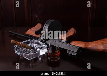 Fusil de sous-machine vintage Thompson sur une table marron foncé avec un cigare et un whisky Banque D'Images