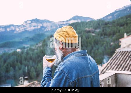 Vue latérale d'un homme heureux contemplant la vue avec une tasse de thé sur un balcon de montagne Banque D'Images