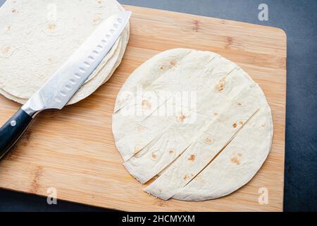 Couper les tortillas de farine en lamelles sur une planche à découper en bambou: Couper les tortillas de farine en lamelles pour faire des chips Banque D'Images