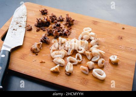 Tubes de calmar cuits coupés en anneaux sur une planche à découper en bambou : tubes de calmar cuits et tentacules sur une planche à découper en bois Banque D'Images