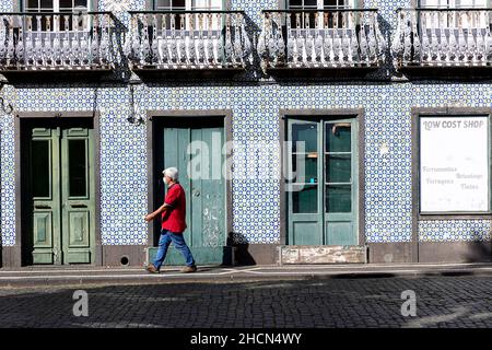 Homme passant par une belle maison traditionnelle couverte de tuiles colorées sur une étroite rue pavée dans la ville de Horta, Faial, Açores, Portugal Banque D'Images