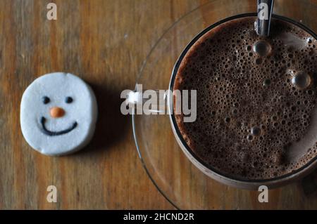 Un chocolat chaud dans une tasse en verre avec soucoupe et un guimauve à visage bonhomme de neige Banque D'Images