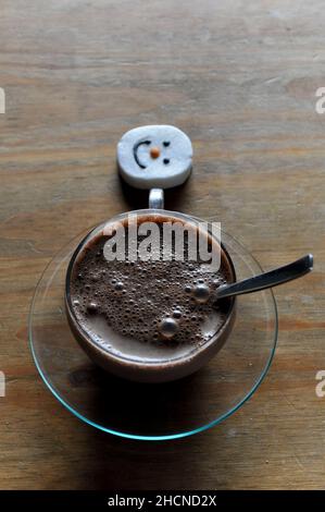 Un chocolat chaud dans une tasse en verre avec soucoupe et un guimauve à visage bonhomme de neige Banque D'Images