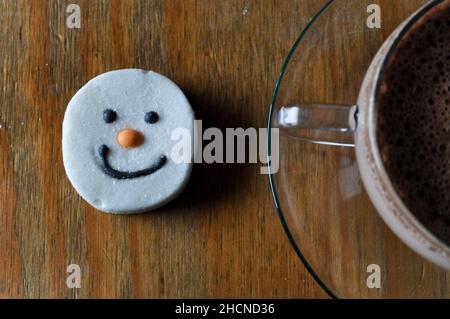 Un chocolat chaud dans une tasse en verre avec soucoupe et un guimauve à visage bonhomme de neige Banque D'Images