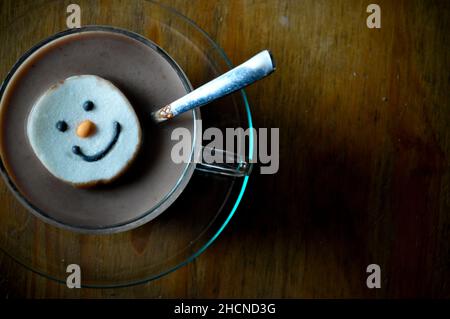 Un chocolat chaud dans une tasse en verre avec soucoupe et un guimauve à visage bonhomme de neige Banque D'Images