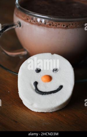 Un chocolat chaud dans une tasse en verre avec soucoupe et un guimauve à visage bonhomme de neige Banque D'Images