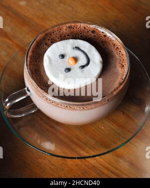 Un chocolat chaud dans une tasse en verre avec soucoupe et un guimauve à visage bonhomme de neige Banque D'Images