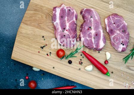 Trois steaks juteux sont à côté des piments rouges et verts, une branche de romarin et d'ail sur une table en bois. Banque D'Images