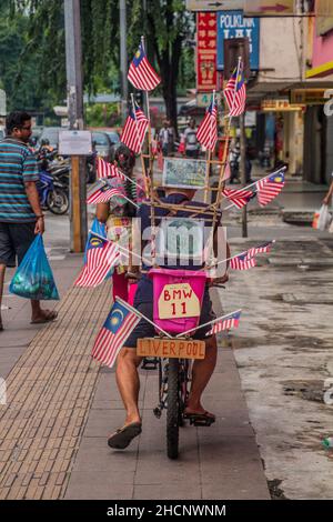 KUALA LUMPUR, MALAISIE - 31 MARS 2018: Homme à vélo avec drapeaux de la Malaisie dans le quartier de Brickfields à Kuala Lumpur, Malaisie. Banque D'Images