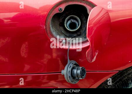 Un bouchon à essence est suspendu à une trappe de remplissage de carburant ouverte sur une voiture rouge. Banque D'Images