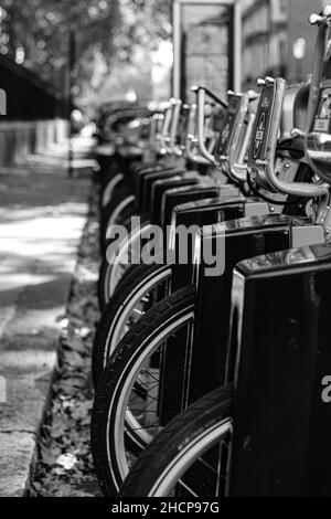 Photo verticale d'une rangée de vélos de location garés près du trottoir, en niveaux de gris Banque D'Images