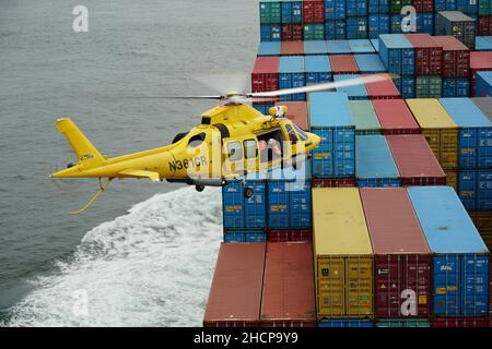 Hélicoptère jaune volant avec un pilote de Columbia River Bar au-dessus de conteneurs. Banque D'Images