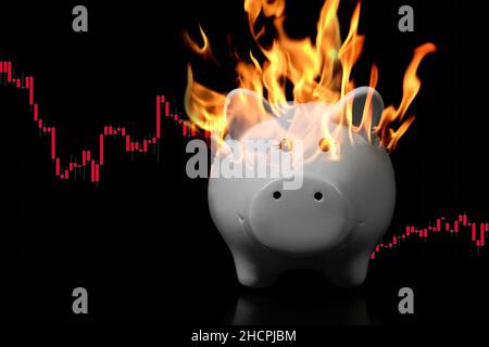 Banc de porc blanc au feu sur une surface très sombre avec tableau rouge descendant des bougies derrière.Concept de crise économique, inflation, dévaluation Banque D'Images