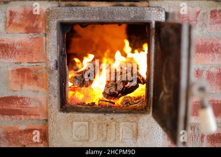 Détails avec feu de bois brûlant à l'intérieur d'un poêle en fer dans l'arrière-cour d'une maison rurale en Roumanie. Banque D'Images