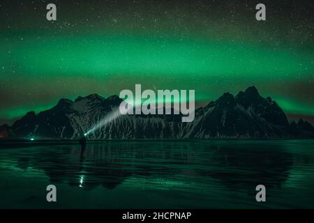 Les jeunes voyageurs se trouvent devant la chaîne de montagnes Vestahorn Stockknes avec aurora borealis et se reflètent sur la plage en Islande.L'un des plus Banque D'Images