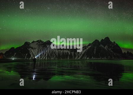 Les jeunes voyageurs se trouvent devant la chaîne de montagnes Vestahorn Stockknes avec aurora borealis et se reflètent sur la plage en Islande.L'un des plus Banque D'Images