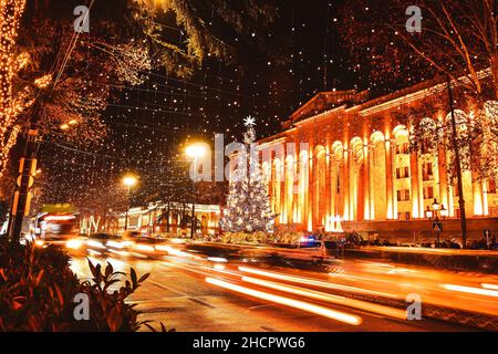 Voitures dans la circulation pendant les heures de pointe la nuit dans l'avenue rustaveli de la capitale Tbilissi en Géorgie sur Noël avec arbre de Noël par le Parlement en arrière-plan Banque D'Images