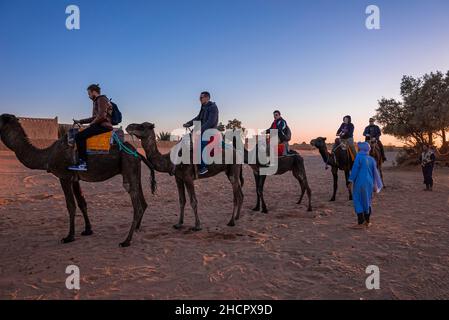 Bédouins en robe traditionnelle debout à côté des touristes montés sur des chameaux à monter à cheval Banque D'Images