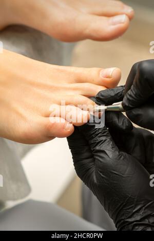 Retrait de la cuticule sur les orteils.Les mains en gants noirs de pédicure maître enlever la cuticule sur les orteils de la femelle par le poussoir Banque D'Images