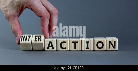 Symbole d'action ou d'interaction.Homme d'affaires tourne des cubes en bois et change le mot action en interaction.Magnifique arrière-plan gris, espace de copie.Buline Banque D'Images