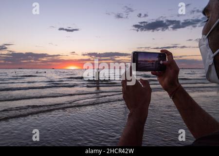 Melbourne, Australie 31 décembre 2021, un homme prend une photo du coucher de soleil le dernier jour de 2021 à la plage de St Kilda, lors d'une nuit qui a vu des événements autour de Melbourne, au cours de laquelle les gens ont vu le nouvel an en faisant la fête et en buvant avec des amis et des feux d'artifice,avec espoir pour un meilleur 2022!Crédit : Michael Currie/Alay Live News Banque D'Images