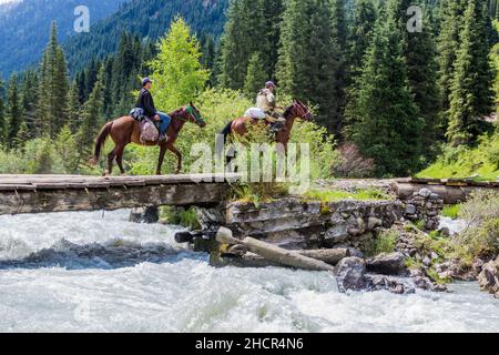 KARAKOL, KIRGHIZISTAN - 16 JUILLET 2018 : des cavaliers locaux traversent un pont au-dessus de la rivière Karakol au Kirghizistan Banque D'Images