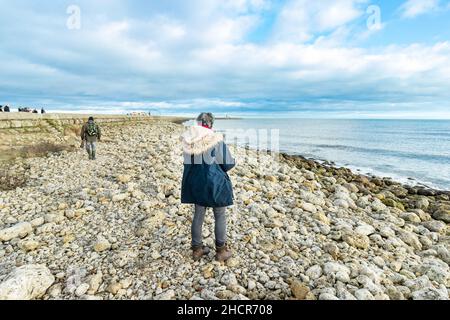 femme marchant sur une plage rocheuse boucliers sud avec une vue sur l'océan sous un ciel partiellement nuageux. boucliers sud Banque D'Images