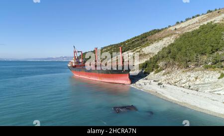 Antenne pour navire de fret rouge industriel sur la rive bleue de la mer avec beaucoup de personnes marchant.Grande barge amarrée sur la rive de la mer près d'une pente recouverte d'un arbre vert Banque D'Images