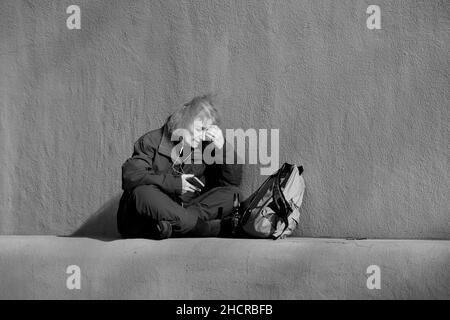 Une femme en visite à Santa Fe, au Nouveau-Mexique, utilise son smartphone tout en étant assise devant le Musée d'histoire du Nouveau-Mexique. Banque D'Images