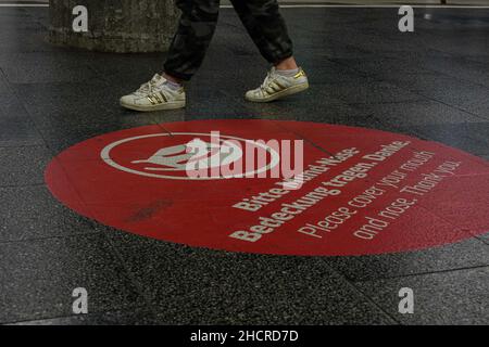 Grand cercle rond sur la plate-forme de la station Marienplatz à Munich avec une demande de couvrir la bouche et le nez.Les pieds des passagers sont visibles. Banque D'Images