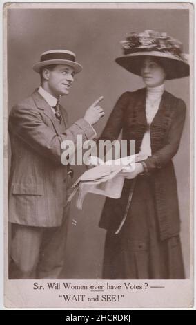 « ir, les femmes auront-elles jamais des votes ?- 'attendez et voyez!'- carte postale photographique montrant une femme dans un grand chapeau décoré pointant vers un journal, un homme dans un boater en paille pointe son doigt vers elle Banque D'Images