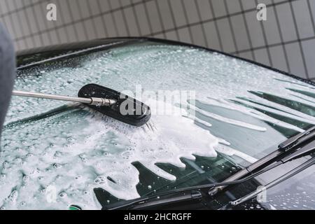 En utilisant une brosse pour laver une voiture sur une installation de lavage de voiture sur la journée d'été ensoleillée Banque D'Images