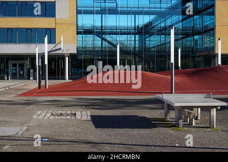 Une table de ping-pong devant un terrain de basket-ball extérieur avec un plancher ondulé rouge devant une école. Banque D'Images