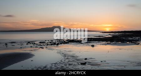 Soleil levant au-dessus des nuages à Milford Beach en été, l'île Rangitoto au loin. Banque D'Images