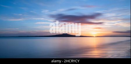 Soleil levant sur l'île Rangitoto à Milford Beach, Auckland. Banque D'Images