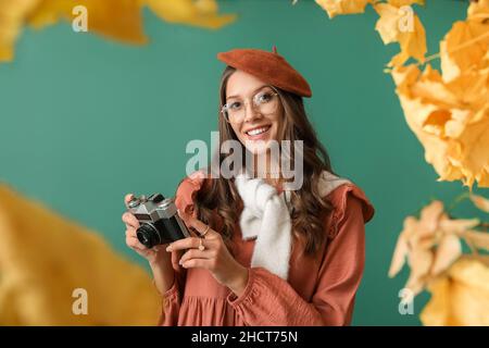 Femme parisienne souriante avec appareil photo vintage dans un cadre en feuilles d'automne sur fond vert Banque D'Images