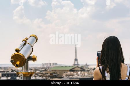 Télescope avec vue sur la Tour Eiffel et femme prenant des photos avec un smartphone à Paris Banque D'Images