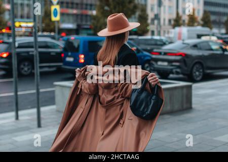 Jeune femme blonde en chapeau beige et long manteau de cuir brun d'automne marchant dans la ville.Mode Street style femme Banque D'Images