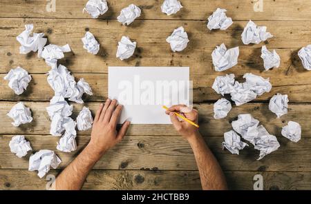 Mains tenant une feuille de papier vierge pour écrire une maquette ou des idées avec un stylo entouré de boules de papier froissés.Image de concept de brainstorming Banque D'Images