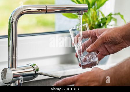 la main verse l'eau dans un verre à partir du robinet de la cuisine Banque D'Images