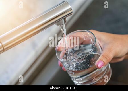 les femmes ont des mains avec du verre et gagnent de l'eau du robinet dans l'évier de cuisine Banque D'Images