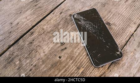 Téléphone mobile moderne avec écran cassé sur fond de bois Banque D'Images