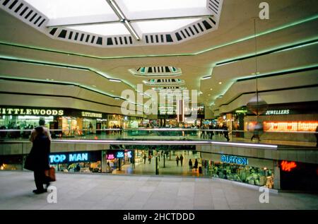 L'intérieur du centre commercial Queensgate, Peterborough, Cambridgeshire, Angleterre, Royaume-Uni en 1985.Le grand centre commercial de centre-ville a été ouvert par la reine Beatrix des pays-Bas le 9 mars 1982.Les détaillants visibles incluent Littlewoods, Burton et Top Man.Le centre compte plus de 100 magasins et un parking de 2 300 voitures dans quatre parkings à plusieurs étages.Cette image provient d'une transparence amateur de 35mm couleurs dans des conditions d'éclairage médiocres, une photographie vintage de 1980s. Banque D'Images