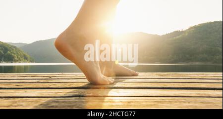 Jambes sur la jetée d'une jeune femme au coucher du soleil. Image du concept de yoga Banque D'Images