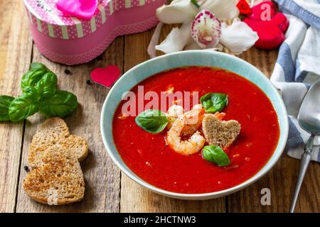 Soupe de Saint-Valentin maison, repas de fête.Soupe de tomates, purée de gazpacho avec tomates, fruits de mer servis sur une table rustique en bois. Banque D'Images