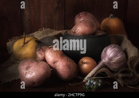 Tubercules de pommes de terre mûrs et autres légumes sur fond de bois foncé dans un style rustique Banque D'Images